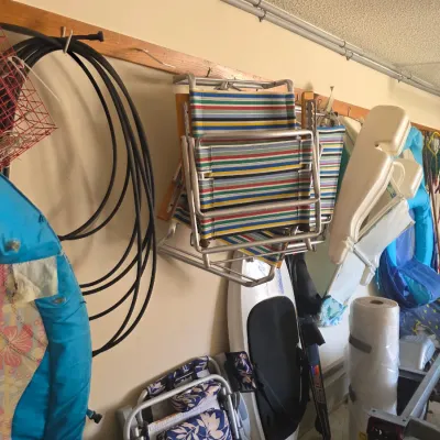 Sale Photo Thumbnail #97: Assorted garage storage items including vintage striped folding lawn chairs, a surfboard, pool floats, and coiled black tubing hanging on a wall rack.