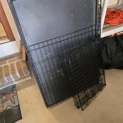 Sale Photo Thumbnail #85: Two collapsible black wire dog crates with removable plastic trays, shown folded flat for storage.