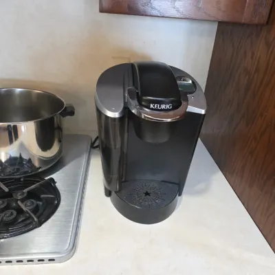 Sale Photo Thumbnail #57: Keurig single-serve coffee maker in black and silver, shown on a kitchen counter next to a stainless steel stockpot.