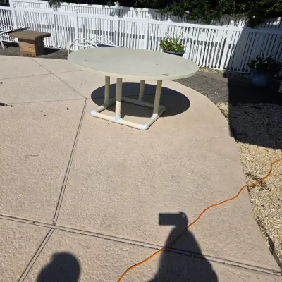Sale Photo Thumbnail #37: Round outdoor patio table with a white fiberglass top and a PVC pipe base, showing some weathering from outdoor use.