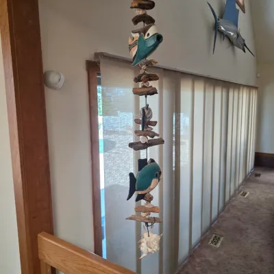 Sale Photo Thumbnail #31: Hanging coastal wind chime featuring carved wooden fish, driftwood pieces, and seashells, suspended in an indoor entryway.