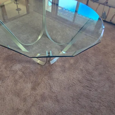 Sale Photo Thumbnail #128: Mid-century modern style coffee table featuring an octagonal, bevel-edged glass top resting on a curved, brushed metal base.