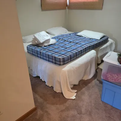 Sale Photo Thumbnail #121: Two twin beds pushed together with white bedspreads, featuring a blue plaid mattress topper, pillows, and folded linens.