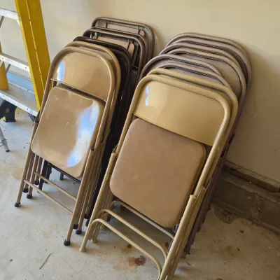 Sale Photo Thumbnail #103: Two stacks of vintage metal folding chairs with tan vinyl padded seats and backs, showing some wear from use.