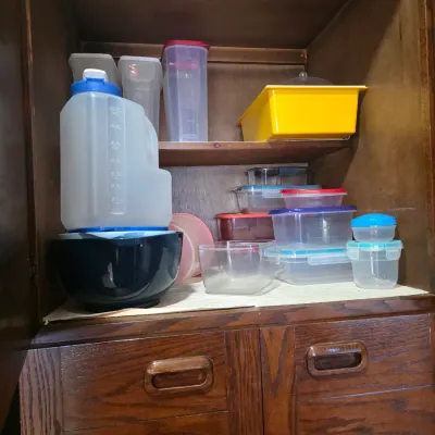 Sale Photo Thumbnail #54: Assorted plastic food storage containers, pitchers, and a mixing bowl, organized inside a vintage wooden cabinet.