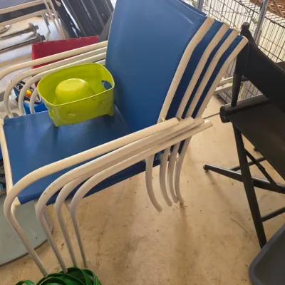 Sale Photo Thumbnail #100: Stack of four vintage outdoor patio chairs with white metal frames and blue vinyl sling seats, accompanied by a lime green plastic pet bowl.