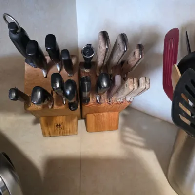 Sale Photo Thumbnail #59: Two wooden knife blocks filled with assorted kitchen knives, including a J.A. Henckels block with black-handled knives and a second block with wooden-handled knives.