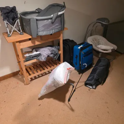 Sale Photo Thumbnail #125: Assorted baby gear and travel items, including a Graco Pack 'n Play, a baby swing, a wooden rolling cart, and rolling suitcases.