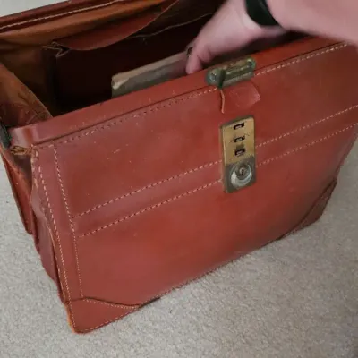 Sale Photo Thumbnail #22: Vintage brown leather doctor's bag or briefcase featuring a brass combination lock and a spacious interior compartment.