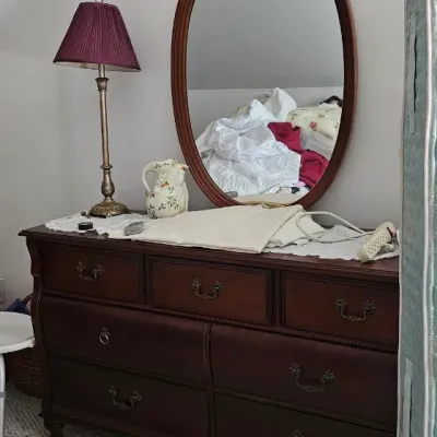 Sale Photo Thumbnail #18: Traditional dark wood dresser featuring seven drawers with ornate brass pulls, paired with a matching oval wall mirror with a carved top crest.