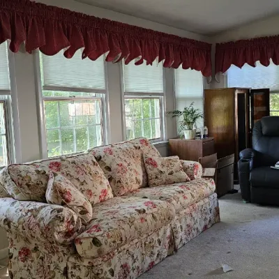 Sale Photo Thumbnail #12: Traditional floral print sofa with matching throw pillows, paired with a black leather recliner in a sunlit living room.