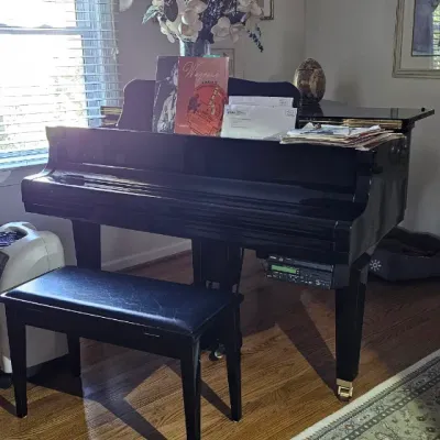 Sale Photo Thumbnail #5: Polished black baby grand piano with a matching padded bench, featuring a player piano control unit mounted underneath.