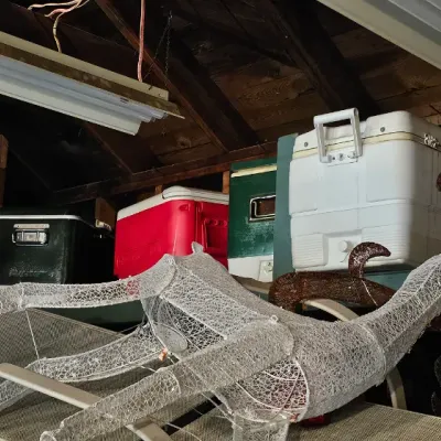 Sale Photo Thumbnail #23: Assorted vintage and modern coolers, including Coleman and Igloo brands, stored in a garage alongside outdoor lounge chairs and wire holiday decorations.