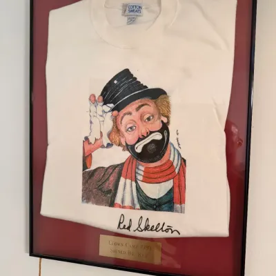 Sale Photo Thumbnail #59: Framed and matted Red Skelton "Clown Camp 1989" sweatshirt, signed by Red Skelton and presented with a commemorative brass plaque.