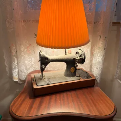 Sale Photo Thumbnail #21: Vintage Singer sewing machine repurposed into a table lamp, featuring a crinkle-finish body, wooden base, and a pleated orange shade.