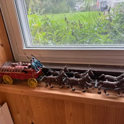 Sale Photo Thumbnail #23: Vintage cast iron Budweiser-style beer wagon toy, featuring a red wagon loaded with barrels, two drivers, and a team of six horses, displayed on a wooden windowsill.