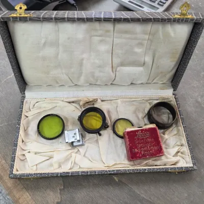 Sale Photo Thumbnail #44: Vintage Leica camera accessories, including yellow filters and a Fipos green filter box, housed in a fabric-lined presentation case.