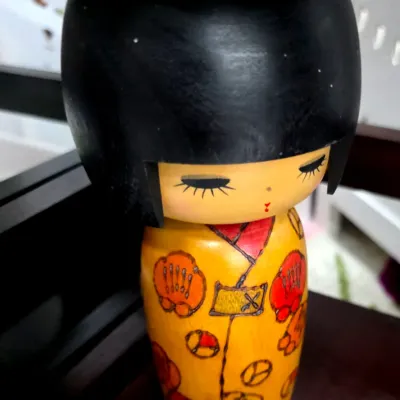 Sale Photo Thumbnail #96: Vintage Japanese Sosaku Kokeshi wooden doll featuring a hand-painted yellow kimono with red floral details and a classic black bob hairstyle.