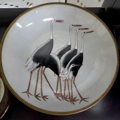Sale Photo Thumbnail #90: Vintage Japanese cloisonné enamel bowl featuring a stylized depiction of five cranes on a pale grey ground with a brass rim.