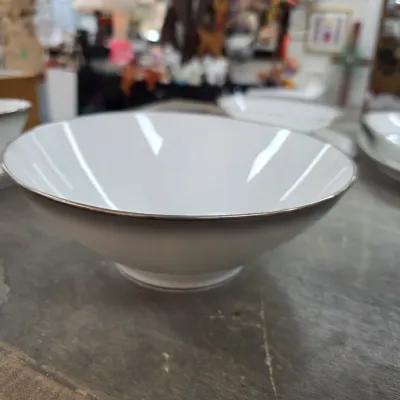 Sale Photo Thumbnail #32: White porcelain serving bowl with a silver-toned rim, displayed on a wooden table.