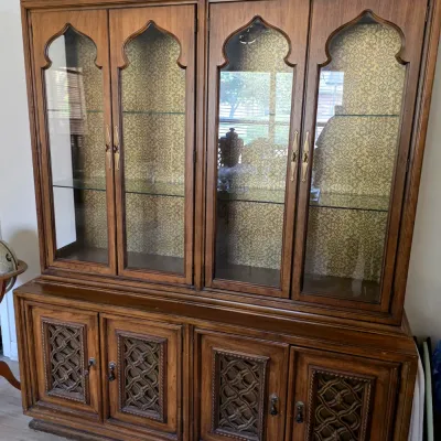 Sale Photo Thumbnail #17: Vintage Mediterranean-style wooden hutch featuring arched glass cabinet doors, glass shelves, a patterned gold backing, and ornate carved lower cabinet doors.