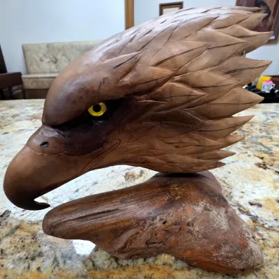 Sale Photo Thumbnail #73: Hand-carved wooden eagle head sculpture mounted on a natural burl wood base, featuring detailed feather textures and a yellow glass eye.