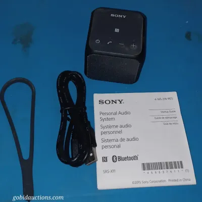 Sale Photo Thumbnail #29: Sony SRS-X11 portable Bluetooth speaker in black, complete with its original USB charging cable, silicone carrying strap, and startup guide.