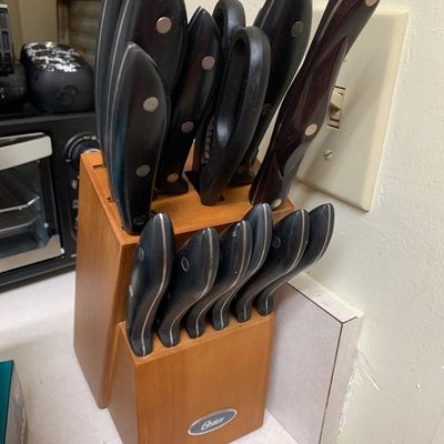 Sale Photo Thumbnail #4: Oster knife set with black handles housed in a two-tier wooden block, showing some signs of use.