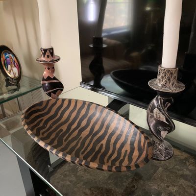 Sale Photo Thumbnail #14: Hand-carved wooden bowl with a zebra stripe pattern, flanked by a pair of African-style carved soapstone candlesticks holding white taper candles.