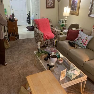 Sale Photo Thumbnail #19: Living room furniture set including a beige leather sofa, a glass-top coffee table with a white frame, and a patterned armchair draped with a pink throw blanket.