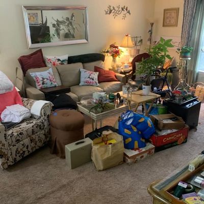 Sale Photo Thumbnail #2: Living room furniture and decor, including a beige leather sofa, floral armchair, brown ottoman, glass-top coffee table, and various household items.