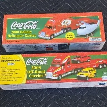 Two Coca-Cola collectible toy trucks in their original boxes, including a 2000 Holiday Helicopter Carrier and a 2003 Off-Road Carrier...