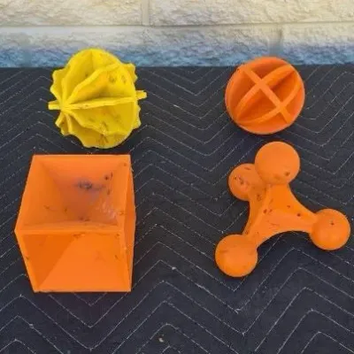 Four vintage orange and yellow rubber dog toys in various geometric shapes, showing some signs of wear and use.