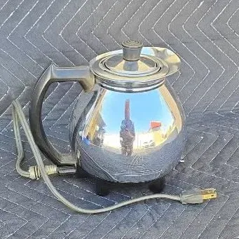 Vintage Revere Ware electric kettle with a polished chrome finish, black plastic handle, and original power cord.