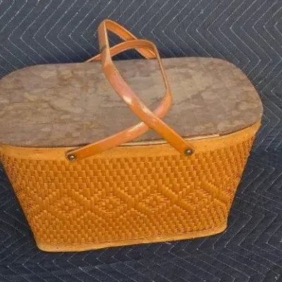 Vintage woven picnic basket with a wooden lid and dual folding handles, showing some wear on the top surface.