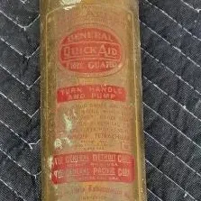 Vintage General Quick Aid brass fire extinguisher with a T-handle pump, showing a weathered patina and original red labeling.