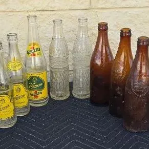 Collection of vintage glass soda bottles, including yellow-labeled Vernors ginger ale bottles, textured clear bottles, and amber glass...