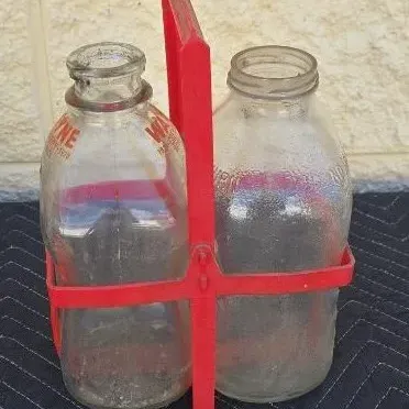 Vintage glass milk bottles, including one with red Wayne Dairy lettering, housed in a red plastic two-bottle carrier.
