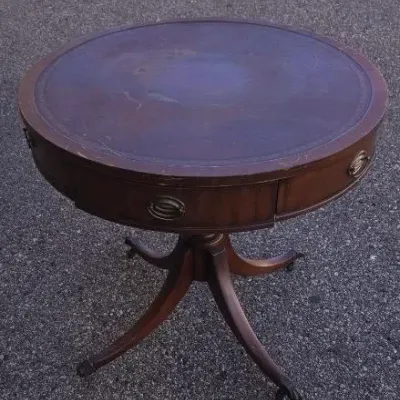 Vintage mahogany drum table featuring a leather-inlaid top with gold tooling, a single drawer with brass hardware, and a pedestal base...