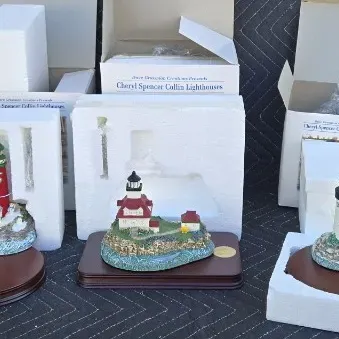 Three Cheryl Spencer Collin lighthouse figurines with wooden display bases, original styrofoam packaging, and boxes.