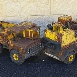 Pair of vintage Tonka pressed steel toy trucks, including a dump truck and a crane truck, showing heavy rust and wear from age.