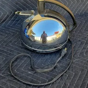 Vintage General Electric chrome electric tea kettle with a black plastic handle and power cord, showing a reflective surface.