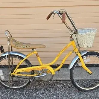 Vintage yellow AMF Roadmaster bicycle featuring a banana seat with floral details, high-rise handlebars, and a front wicker basket.