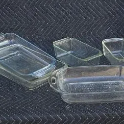 Assorted vintage clear glass baking dishes, including rectangular casseroles and loaf pans, displayed on a dark quilted moving blanket.