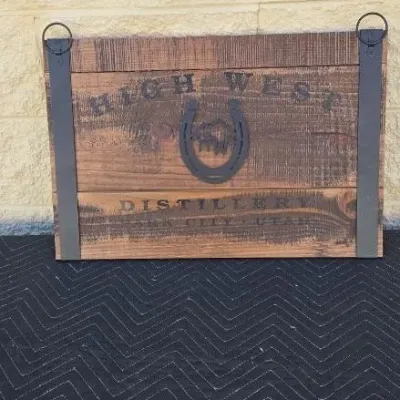 Rustic wooden sign featuring the High West Distillery logo, constructed from reclaimed wood planks with metal strap accents and a central...