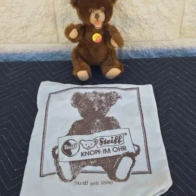 Vintage Steiff brown teddy bear with original ear tag and chest tag, accompanied by a branded Steiff cloth storage bag.