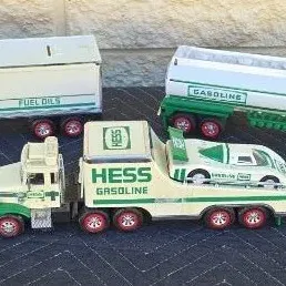 Three vintage Hess toy trucks, including a box trailer, a gasoline tanker, and a flatbed transport truck carrying a race car, showing...