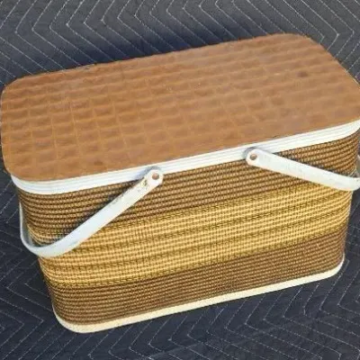 Vintage Redmon picnic basket featuring a woven body in shades of brown and gold, a textured faux-wood lid, and dual white metal handles.