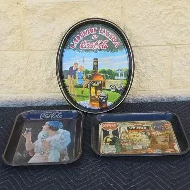 Three vintage advertising trays, including an oval Calvert Extra and Coca-Cola tray and two rectangular Coca-Cola trays featuring retro...