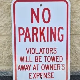 Vintage metal "No Parking" sign with red lettering on a white background, warning that violators will be towed.